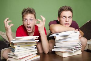 Two teenagers with stacks of homework feeling overwhelmed
