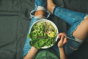 Female teenager sat on floor eating a vegan salad