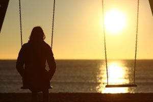 Woman sitting alone on a beach with her negative thoughts watching the sunset.