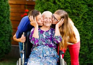 Lady in wheelchair kissed by grandchildren