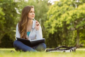 Thinking student sitting and holding book in park at school