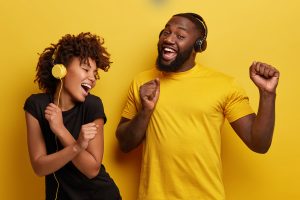 A young man and woman dancing with headphones on in front of a yellow background.