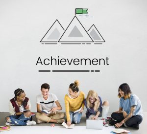 Group of student sitting under a sign saying "Achievement"