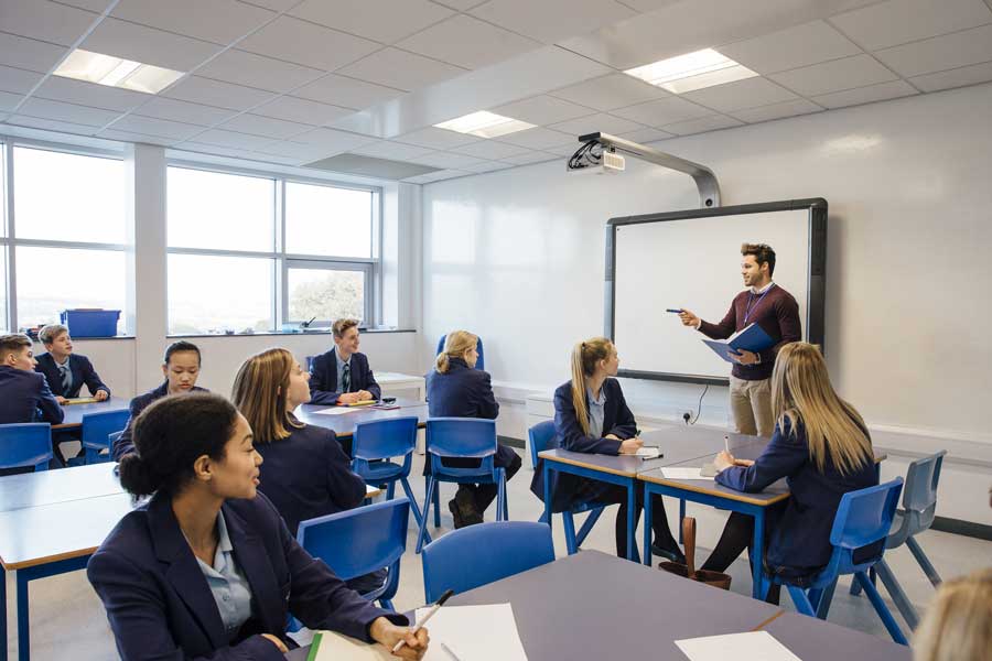 Teacher stands in classroom of happy pupils
